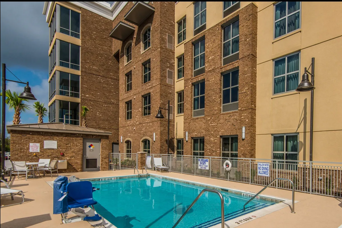 A wide exterior view of the swimming pool featuring the surrounding architecture and ample poolside seating. The pool area looks serene and well-maintained, ideal for both dynamic gatherings and quiet moments by the water.