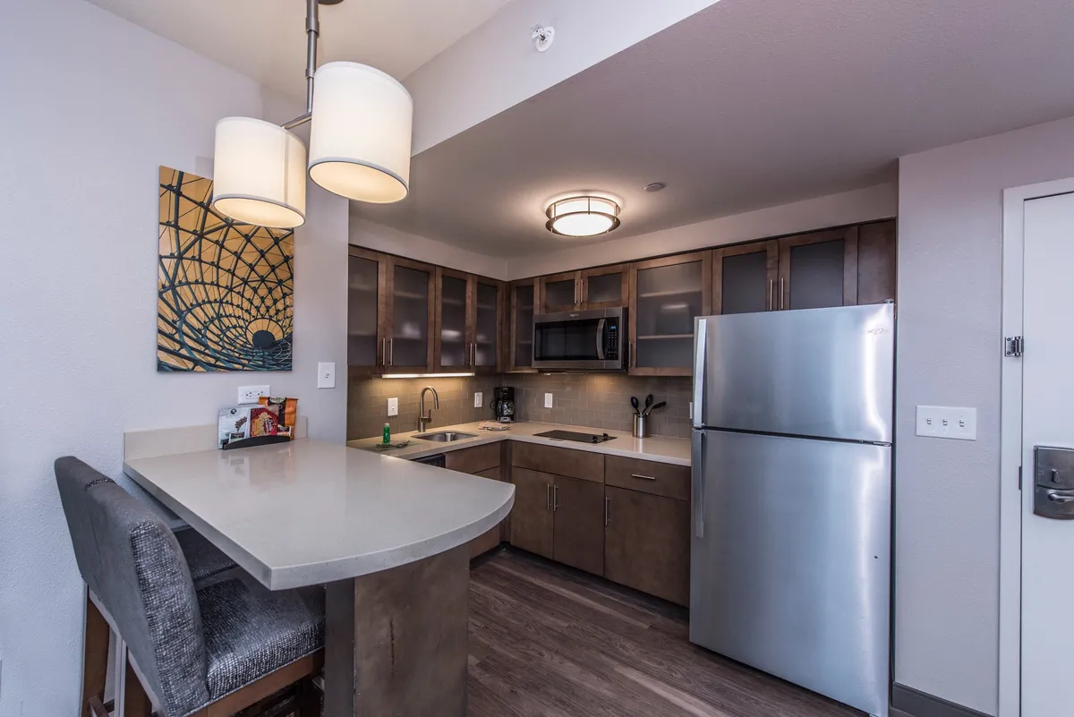 The image showcases a welcoming and comfortable interior space centered around a kitchen island, with modern appliances and vibrant artwork. The scene is set for cooking, entertaining, and socializing, with ample seating at the bar for group conversations and shared meals.