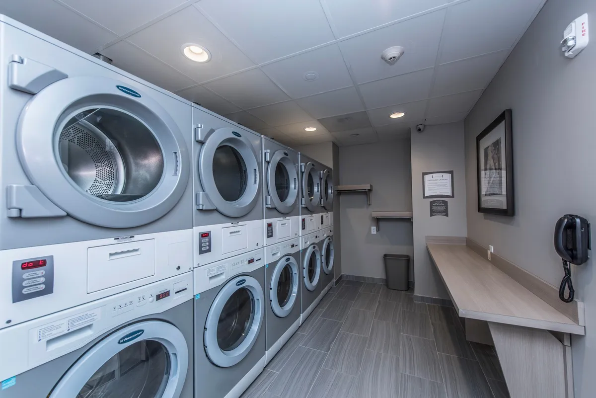 A practical laundry room with stacked washing machines, a folding counter, and a telephone. The scene conveys convenience and efficiency, catering to guests on extended stays who require self-serve laundry options.