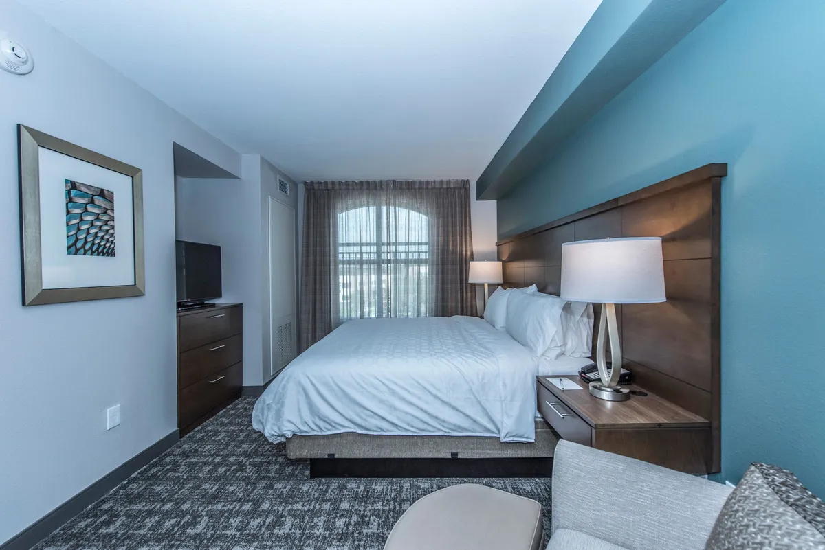 This cozy bedroom scene features a comfortable bed, armchair, bedside lamp, and a television. Sunlight streams in, creating a peaceful retreat for relaxing, reading, or unwinding after a day of exploring Charleston’s vibrant event scene.