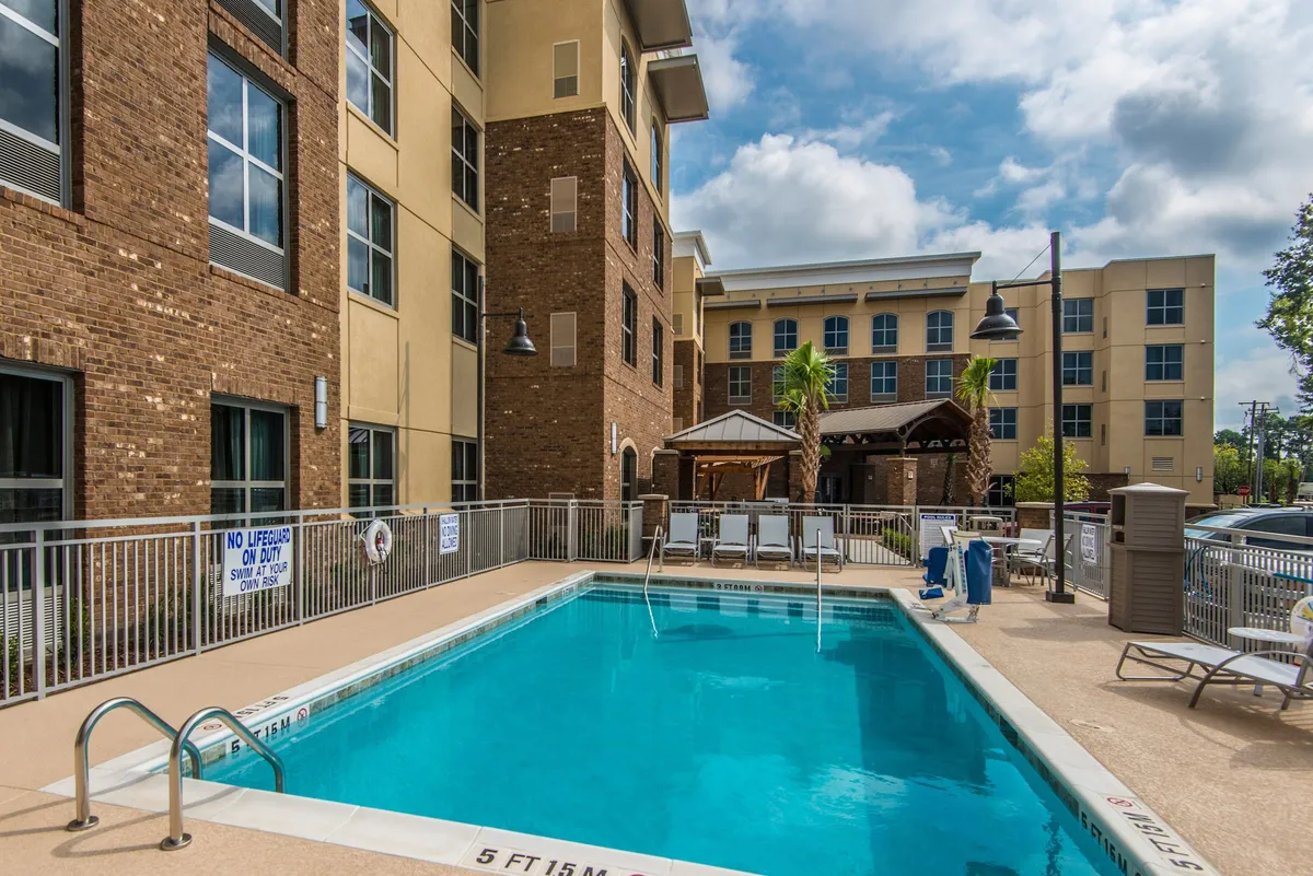 This image captures the inviting outdoor swimming pool surrounded by comfortable lounge chairs and palm trees. The scene shows guests swimming, sunbathing, and socializing, with the pool deck set against the backdrop of the property’s buildings.
