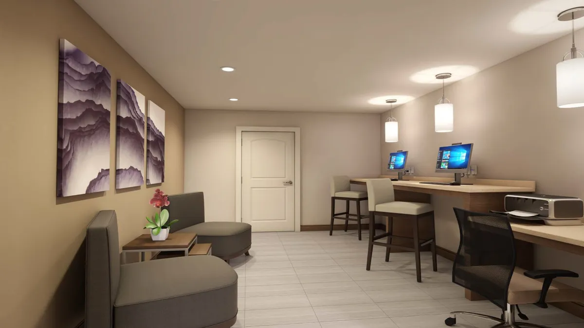 A multifunctional space showcasing computer workstations, an abstract mountain artwork, and a comfortable seating area. The environment is productive yet inviting, accommodating both focused work and informal socializing.