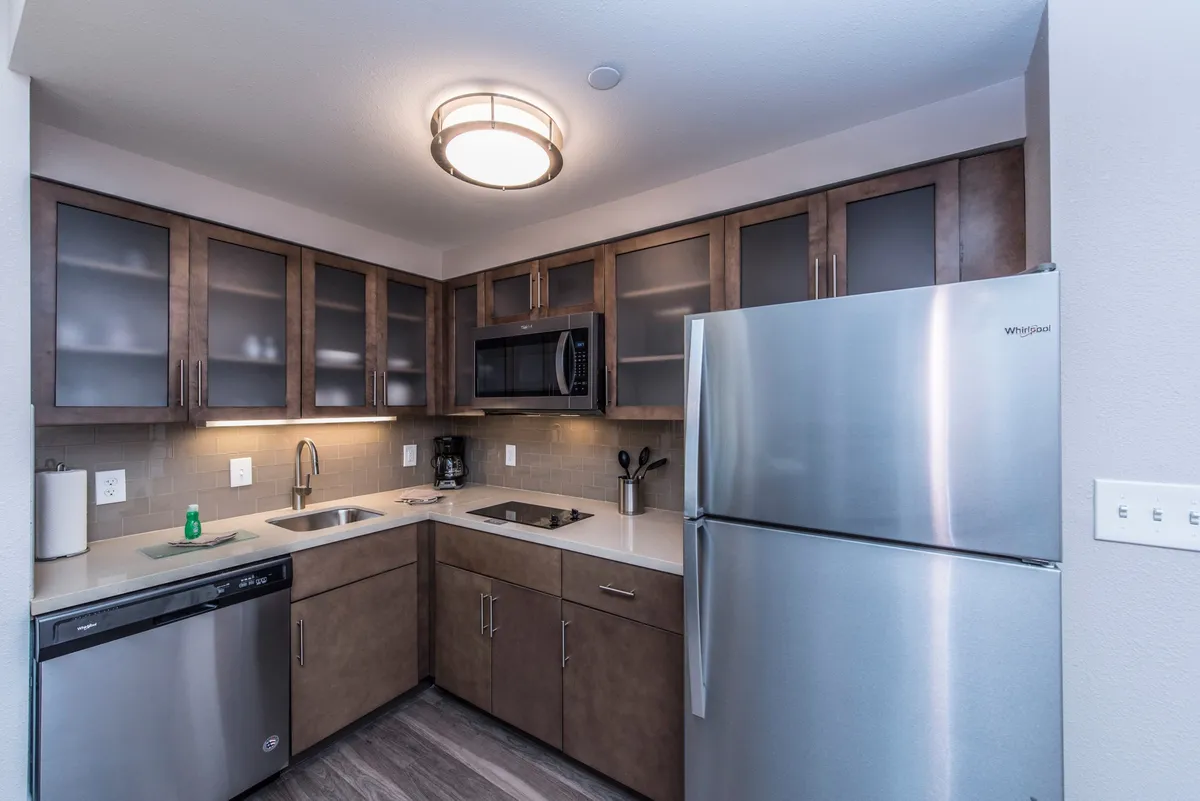 A contemporary kitchen featuring stainless steel appliances, dark wood cabinetry, ample countertops, and a modern lighting fixture. The space is well-equipped for cooking, entertaining, and enjoying meals together.