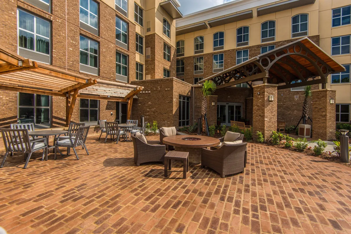 A welcoming exterior scene featuring a fire pit surrounded by comfortable outdoor seating, all set within beautifully landscaped greenery. The inviting layout encourages groups to gather and relax, while the lush surroundings add a touch of natural tranquility.